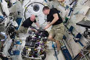 Two astronautes working together to assemble and install equipment
