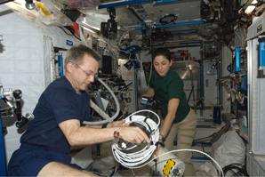 Two astronautes working together on ISS, checking assembly of equipment