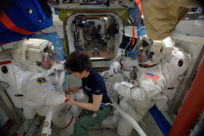 One astronaut helping two other astronauts don space suits