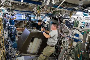 Two astronauts working collaboratively to move a modular equipment rack