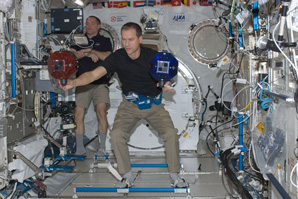 Astronaut spots second astronaut operating floating robot to maintain situational awareness